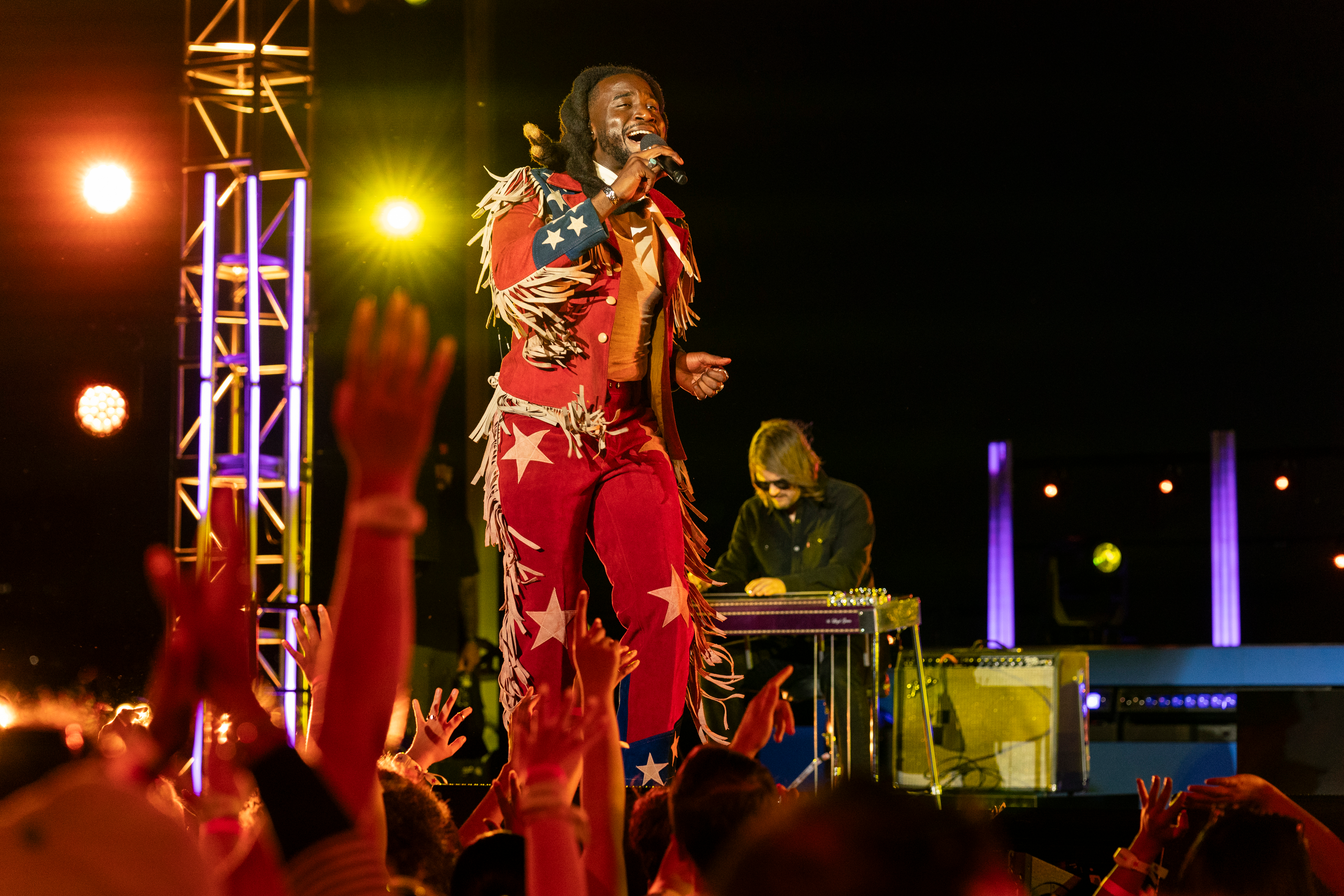 Shaboozey performing on stage in a fringed red and white star-spangled suit.