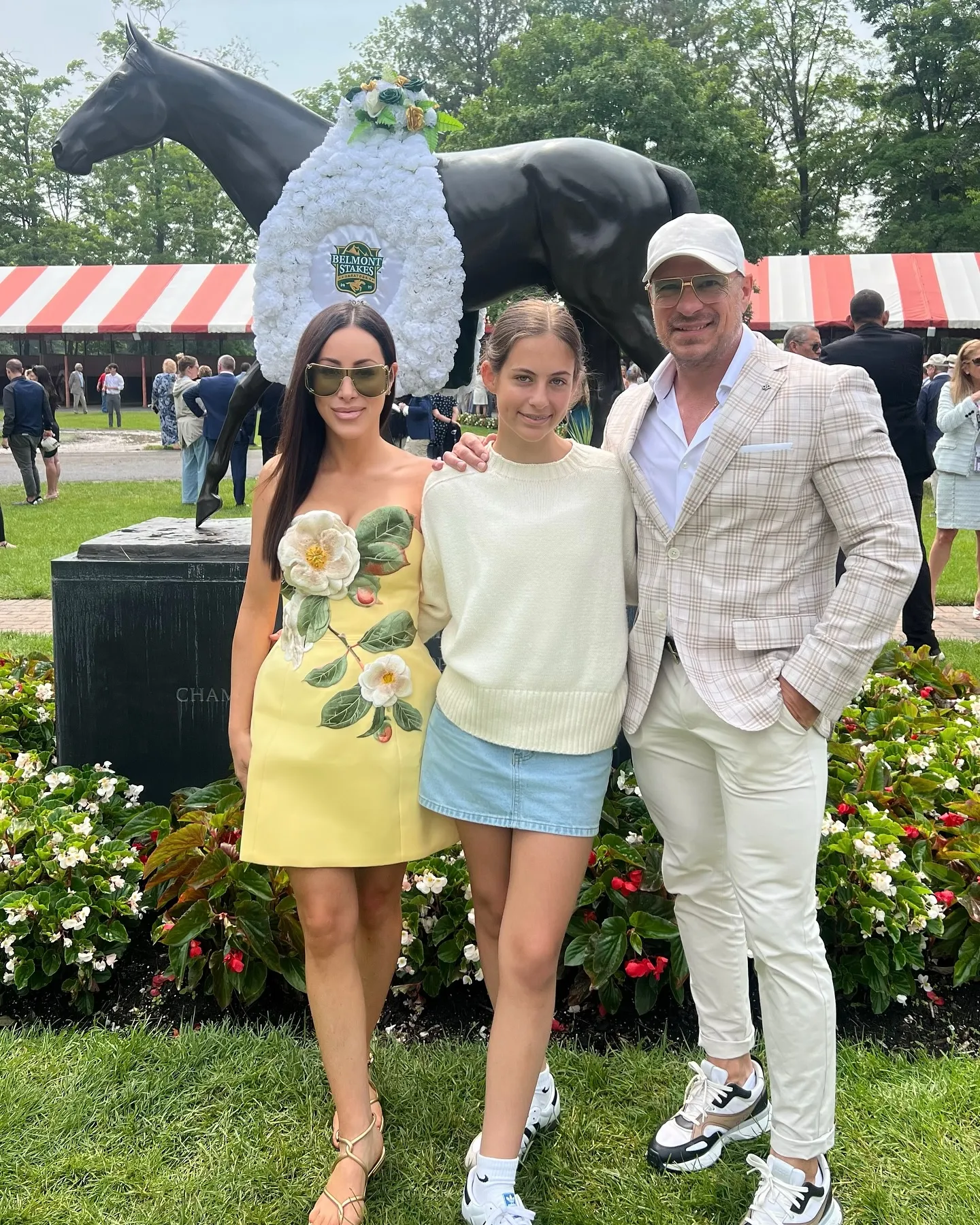 Shawn Trujillo, Elektra Katsanevas, and Angie Katsanevas pose for a photo with a horse statue wearing a Belmont Stakes wreath.