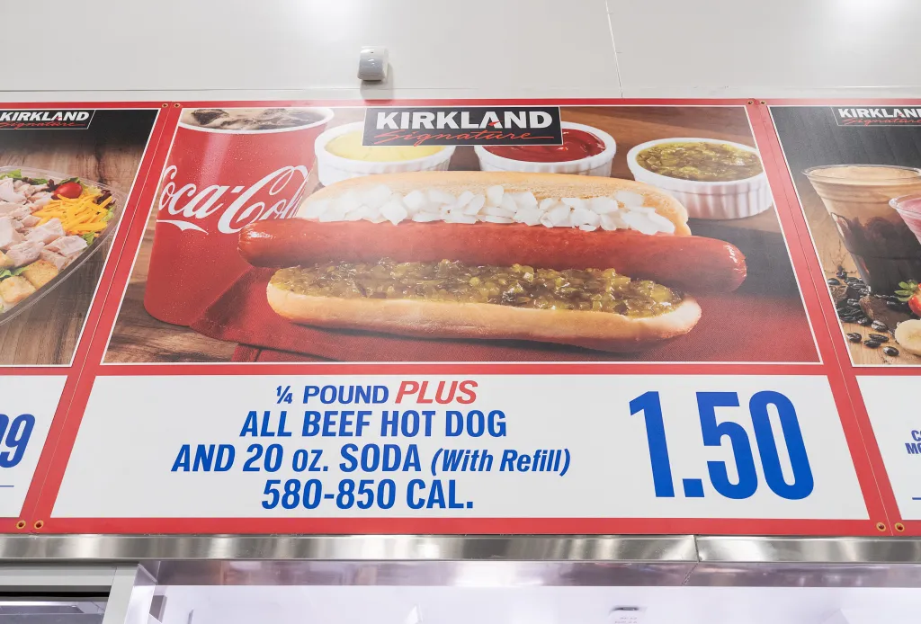 A Costco sign advertising a 1/4 pound all-beef hot dog and 20 oz soda for $1.50, with an image of the hot dog, condiments, and soda.
