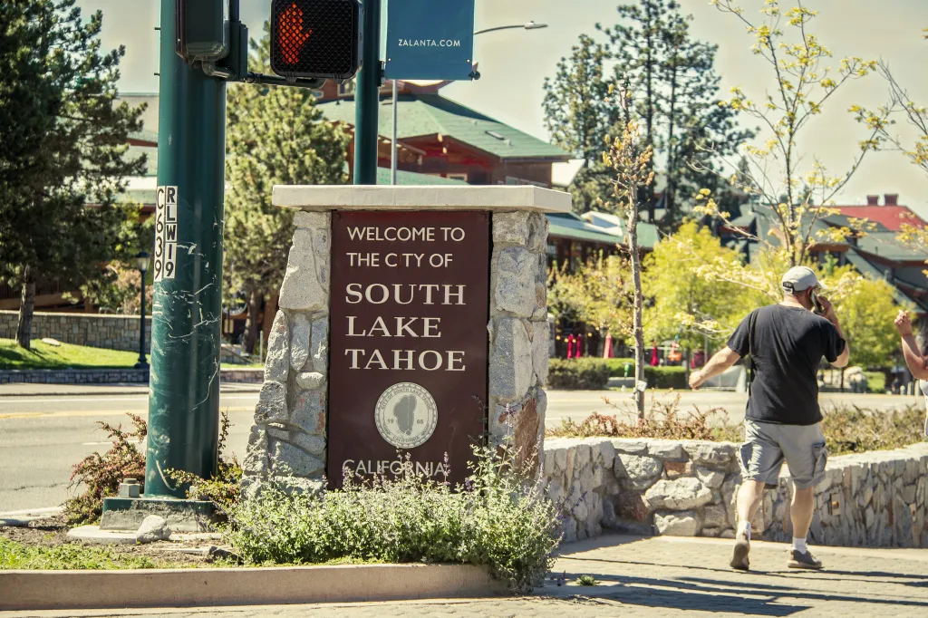 Welcome to South Lake Tahoe sign with a man on his phone walking past.