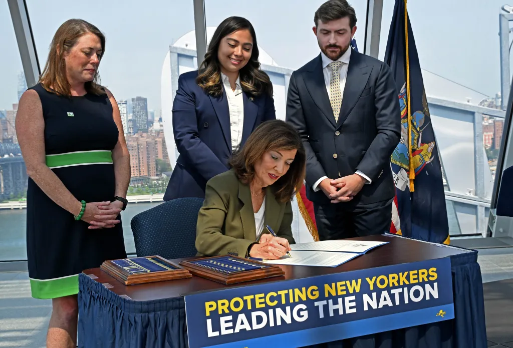 Governor Kathy Hochul signing an executive order to pause AI data center construction, with Julie Tighe, State Senator Kristen Gonzalez, and Coner Eckert in the background.