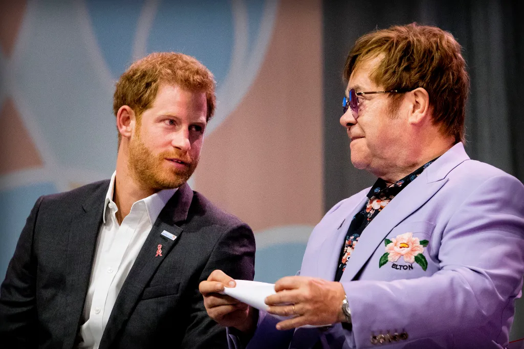 Prince Harry, in a black suit with a red AIDS ribbon, and Elton John, in a purple suit and black floral shirt, attending the International AIDS Conference.