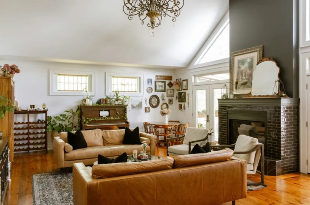A large living room with hardwood floors, a dark gray fireplace, light brown leather sofas, and an ornate chandelier.