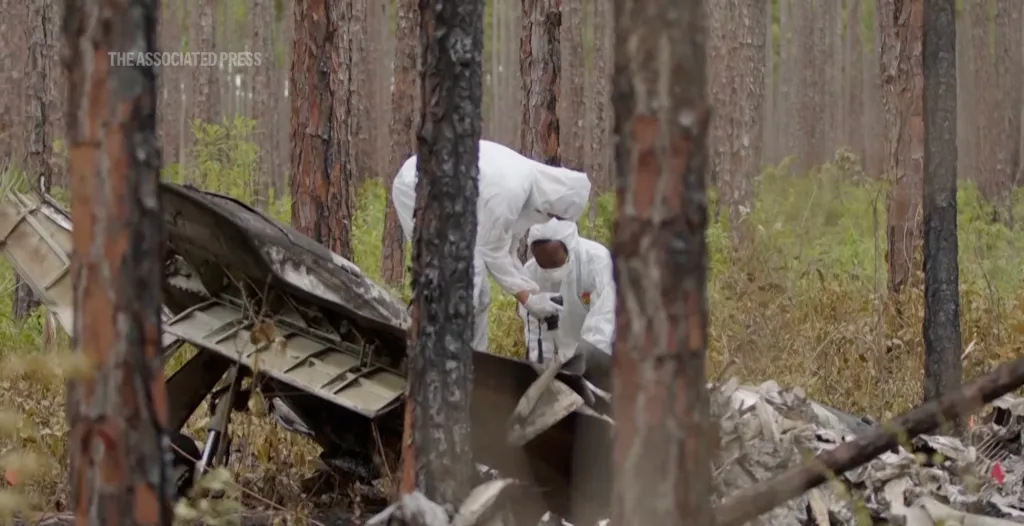 Investigators in hazmat suits examining wreckage from a small plane crash in a forest.