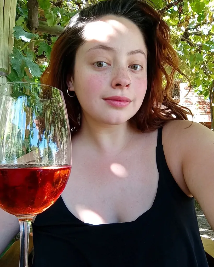 Sofía Devries, a young woman with freckles, looks at the camera while holding a glass of red wine.