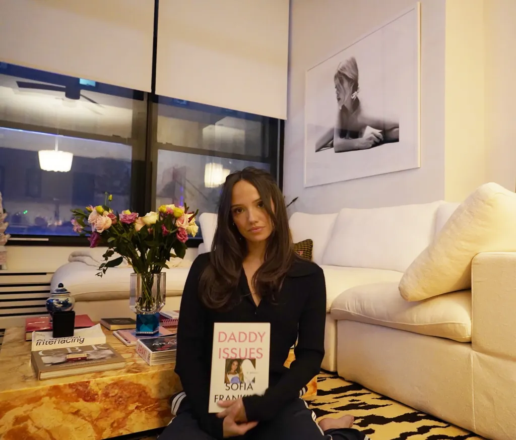 Sofia Franklyn, in a black top and black sweatpants, holding her book