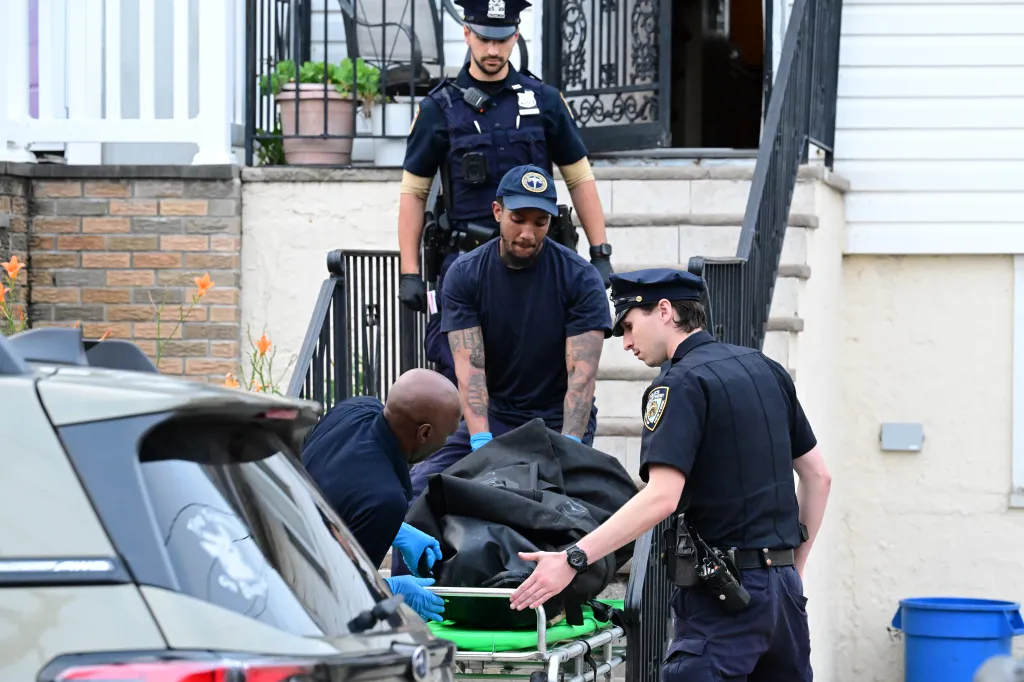 Police and EMS workers remove a body covered in a black bag from a house on a stretcher.