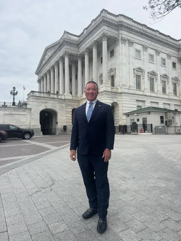 TecFusion CTO Simon Tusha stands smiling in front of a large, white classical building with columns.