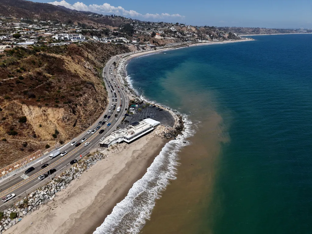 Aerial view of Topanga State Beach, showing a stretch of highway, a building, and the ocean with a cloudy, brown area near the shore due to bacteria.