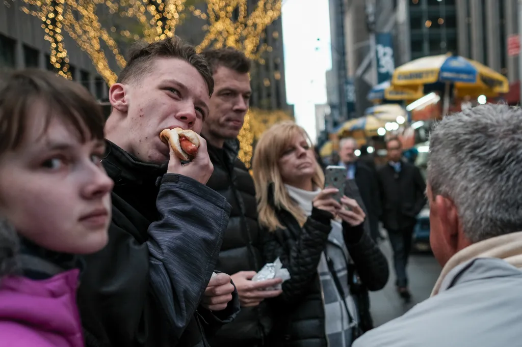 People eating hot dogs from a street vendor in New York City.
