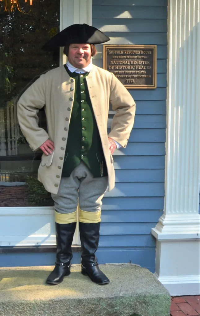 Paul Revere reenactor Michael Lepage in colonial attire standing next to a house with a plaque that reads 