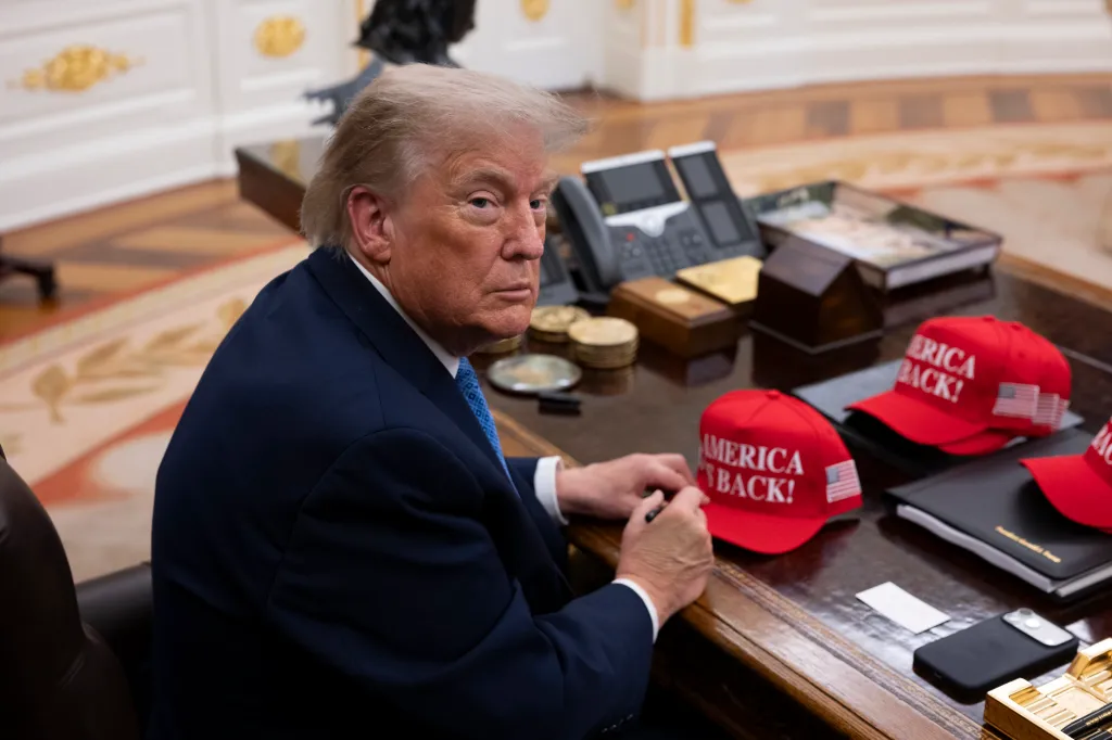 Donald Trump signing red hats that say 