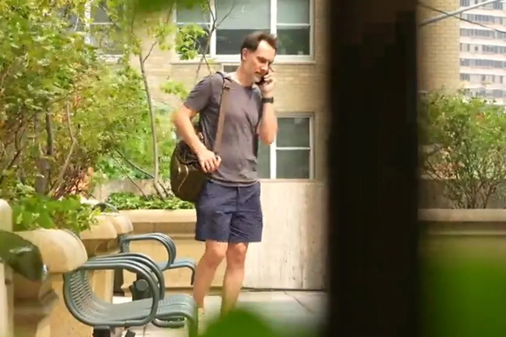 Josh Felker, wearing a gray shirt and dark shorts, talking on a phone with a brown messenger bag over his shoulder.