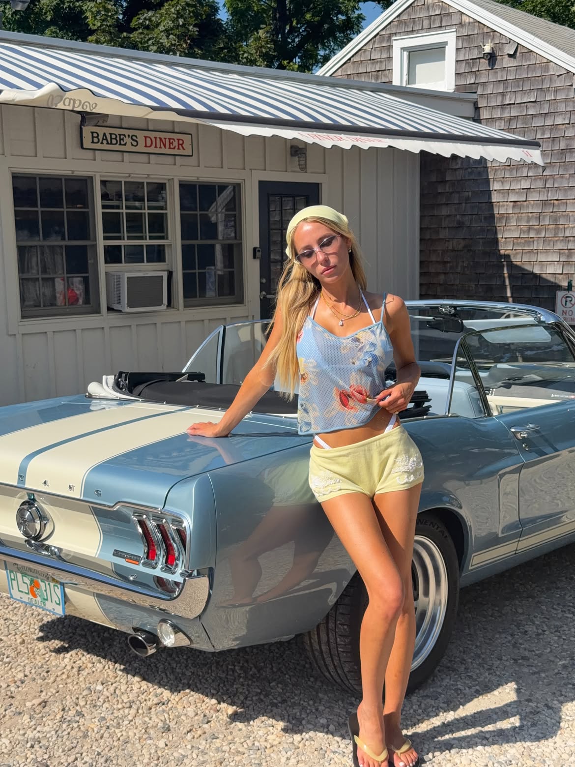 Alix Earle posing next to a light blue Ford Mustang convertible with white racing stripes in front of 