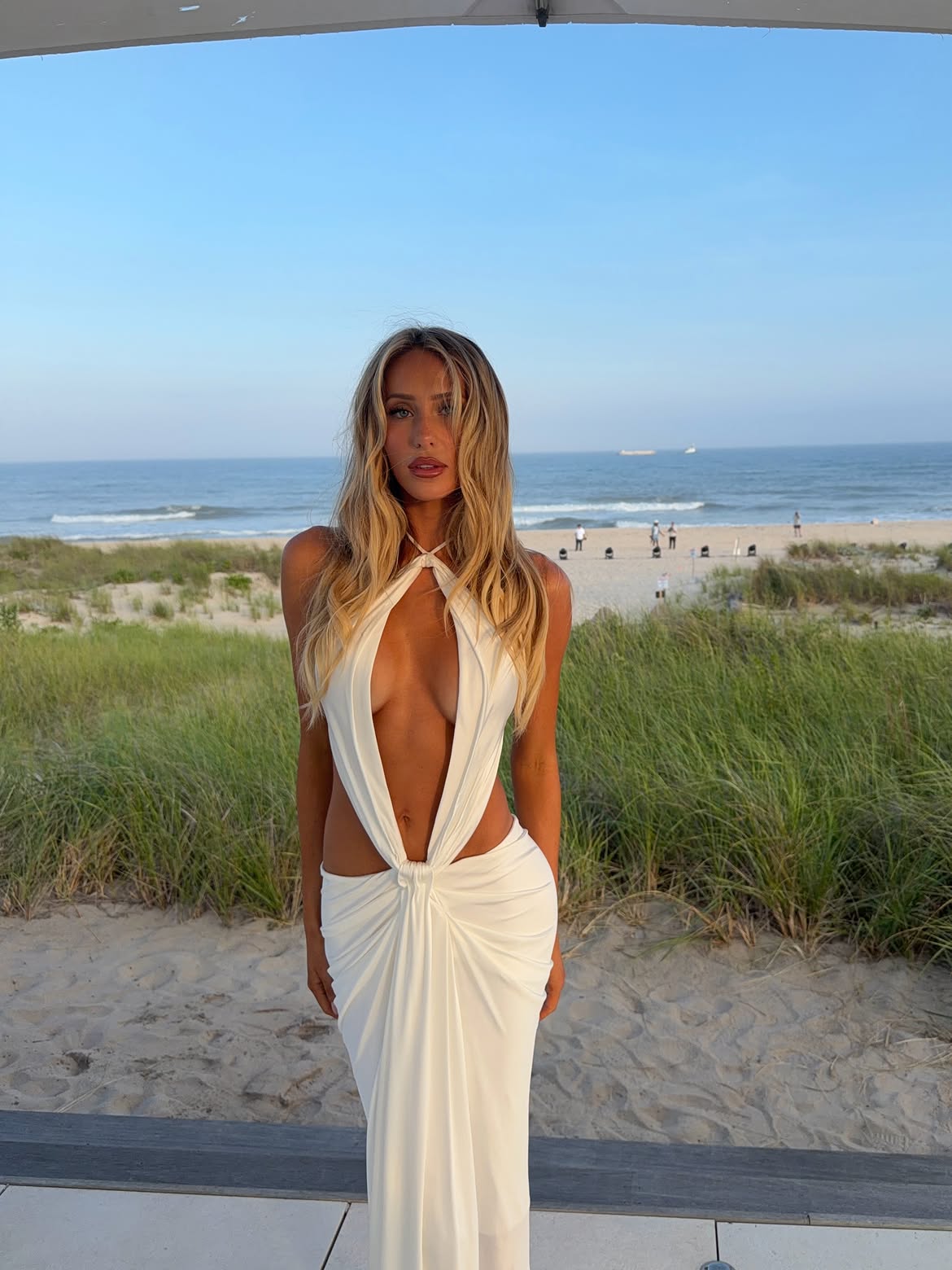 Alix Earle wearing a white cutout dress at the beach.