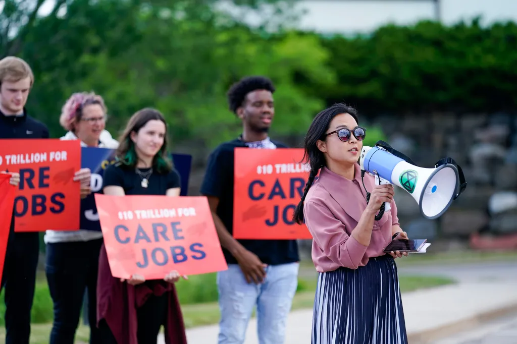 Wisconsin State Rep. Francesca Hong speaks into a megaphone, with protestors behind her holding signs that read 