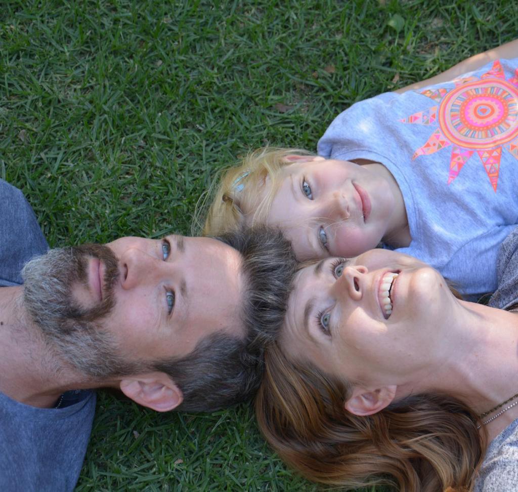 A family of three, including a man, woman, and young girl, lying on grass.