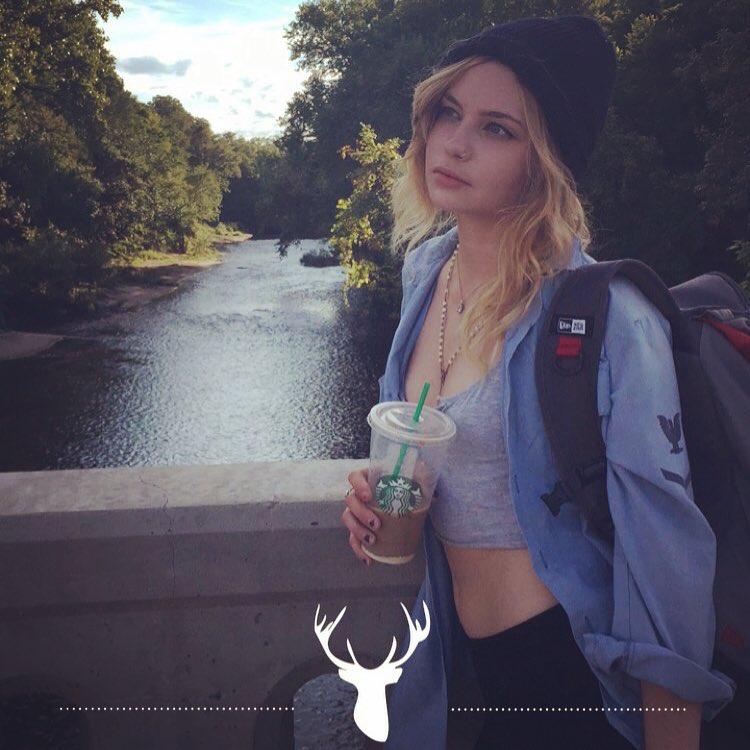 Daveigh Chase on a bridge with a coffee, a river behind her.