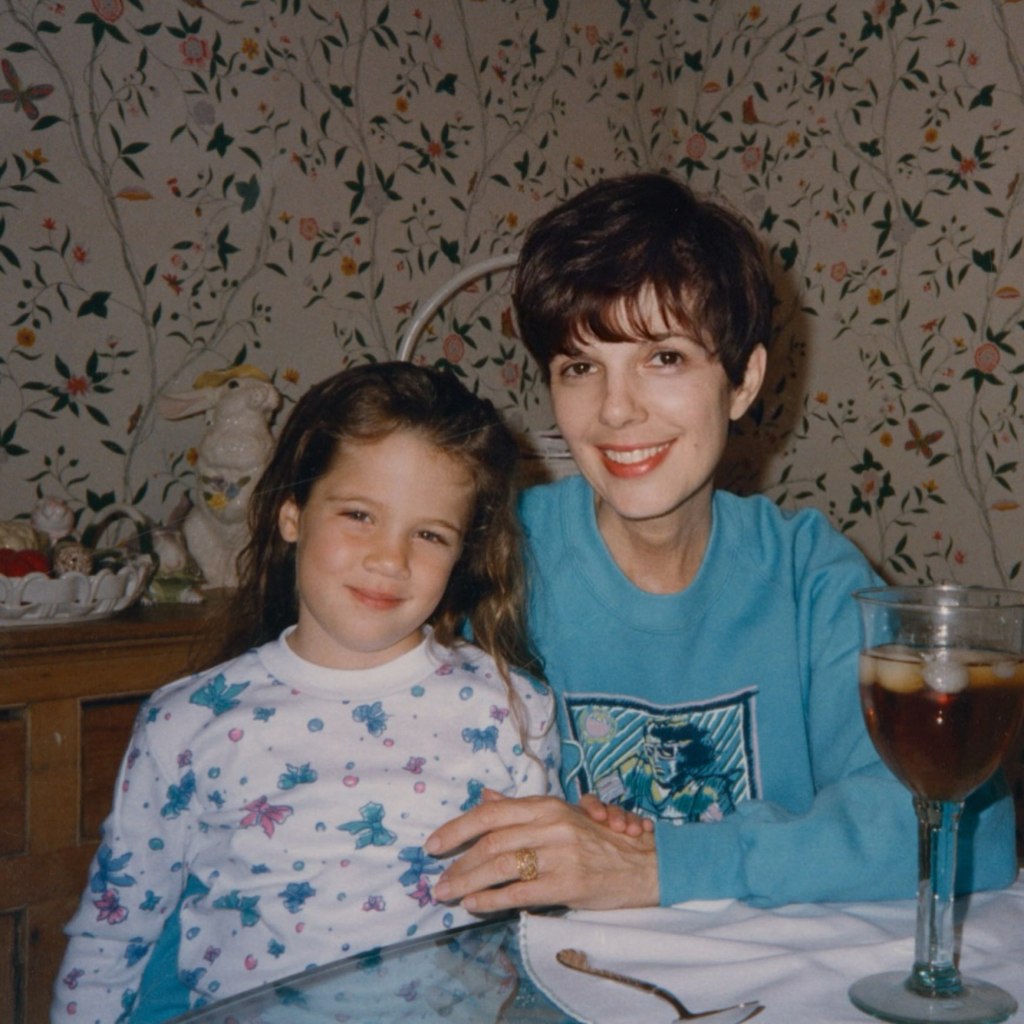 A young girl with long brown hair and a woman with short brown hair sit at a table, smiling at the camera.