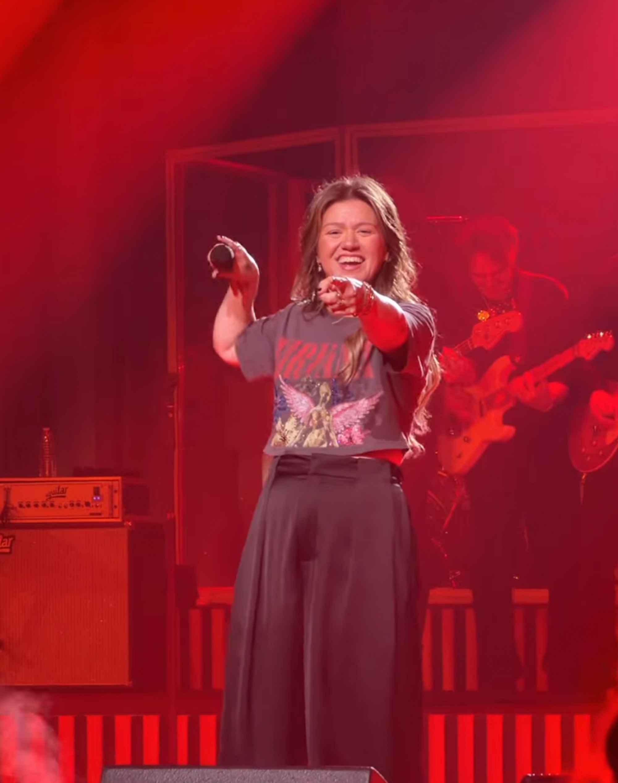 Kelly Clarkson performing on stage under red lights.
