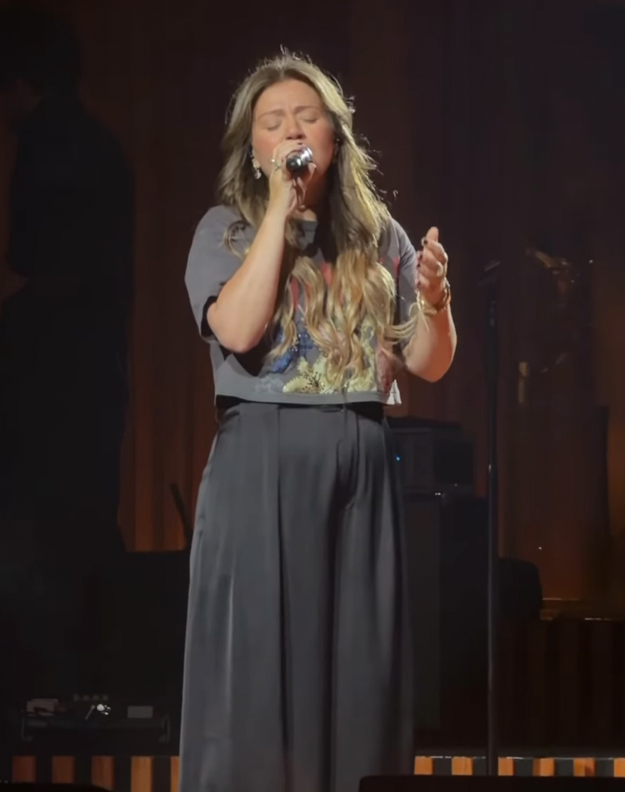Kelly Clarkson singing into a microphone on stage during a performance.