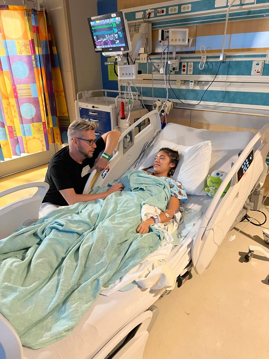 Kenny sitting by Hannah's hospital bed.