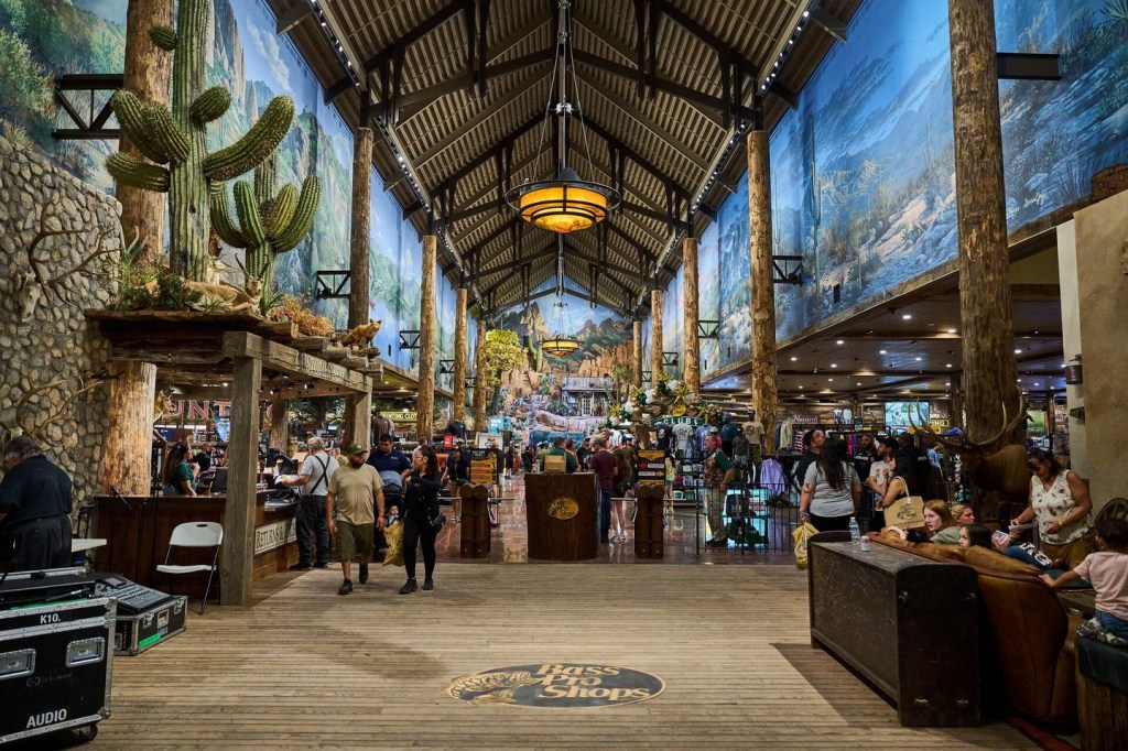 Bass Pro Shops interior with high ceilings, large scenic wall murals, and artificial cacti and animal displays.