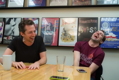 Two men laughing, one in a black shirt and one in a maroon t-shirt with 