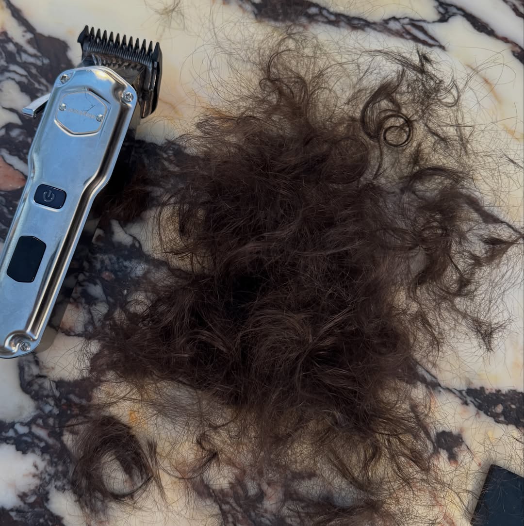 A pile of dark hair and a hair clipper on a marble surface, representing a child's hair being shaved due to cancer treatment.