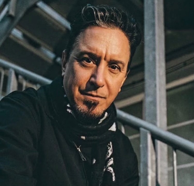 Headshot of Lou Koller with a short goatee and dark hair, wearing a black jacket and a black and white scarf.