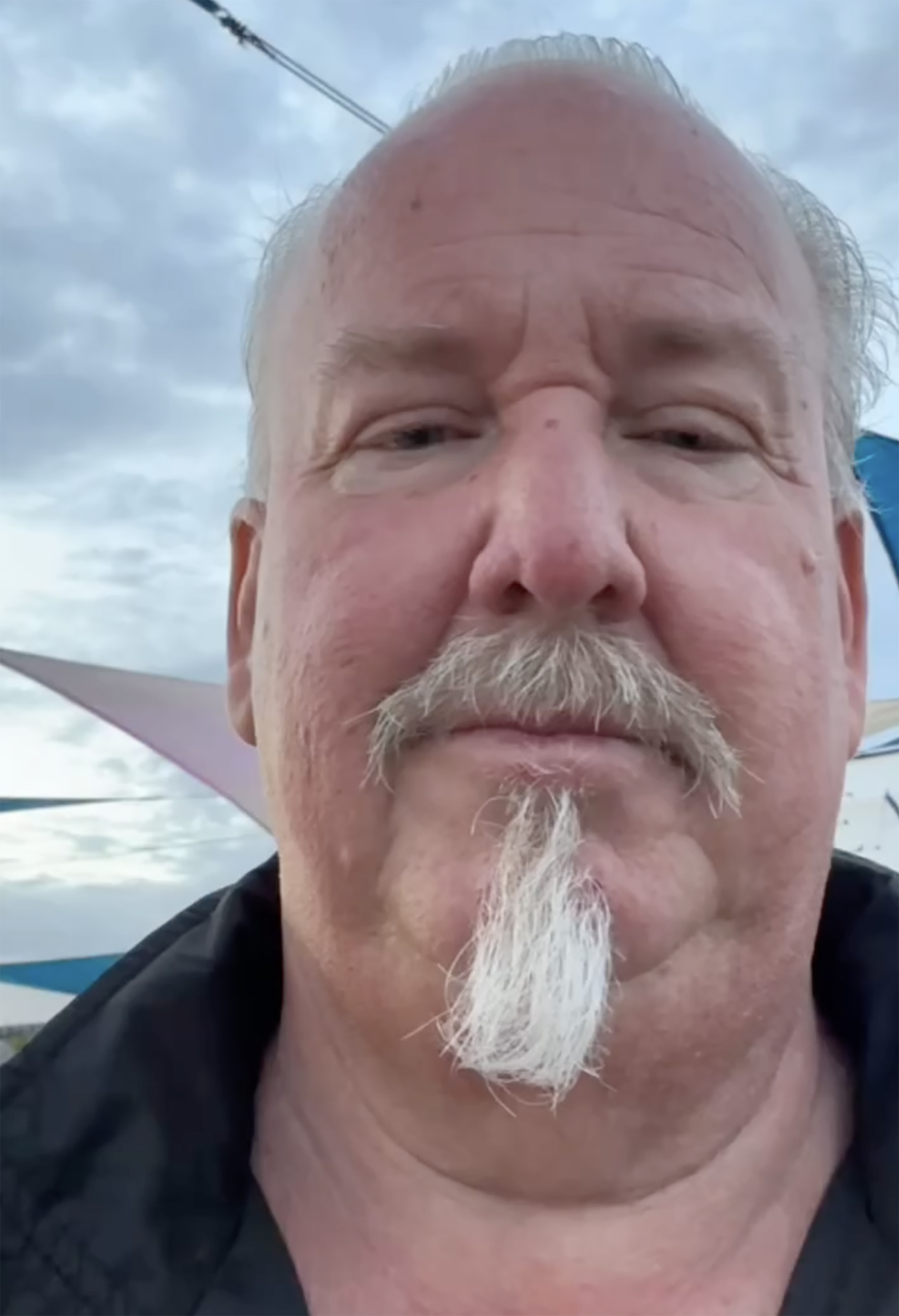 Darrell Sheets, a white man with gray hair, mustache, and goatee, wearing a black shirt, looks directly at the camera.