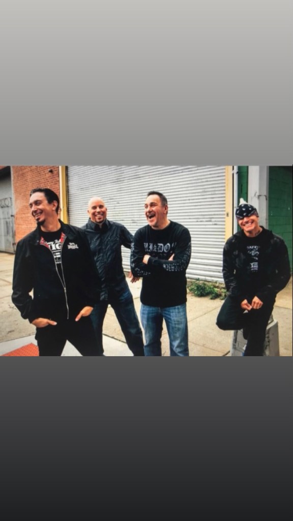 Four men, including Lou Koller of Sick Of It All, laughing on a street.