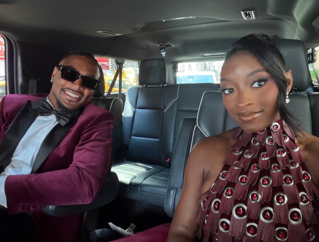 Simone Biles and a man dressed in formal wear sit in the back of a car.