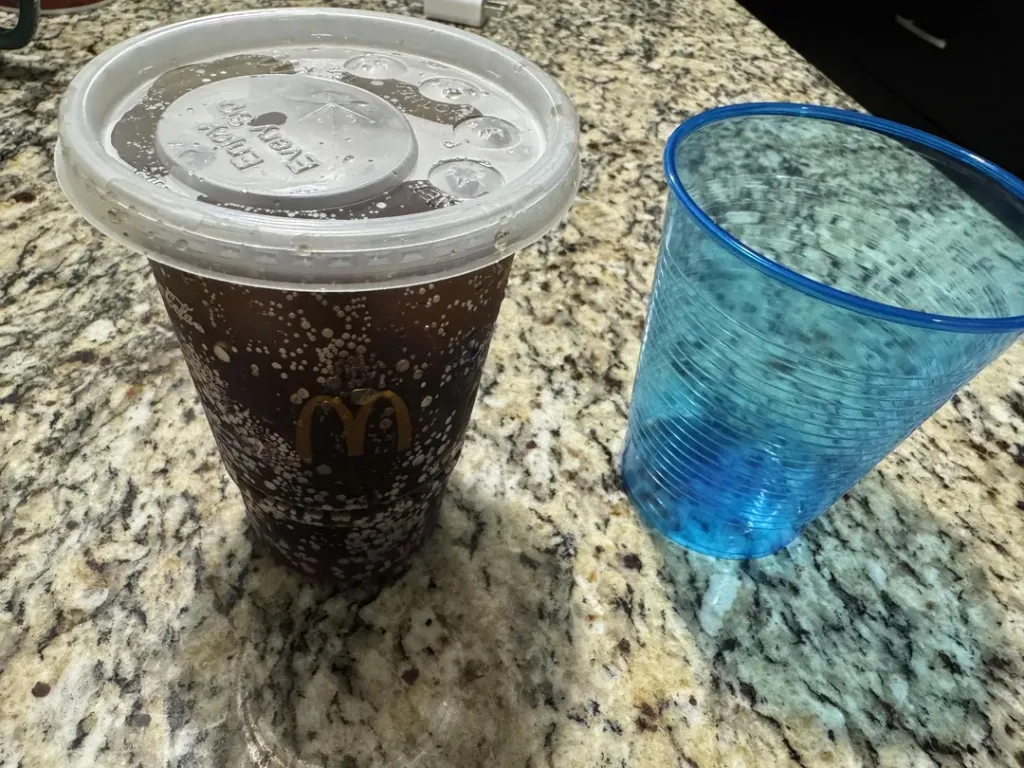 McDonald's small Coke with a lid, next to an empty blue plastic cup.