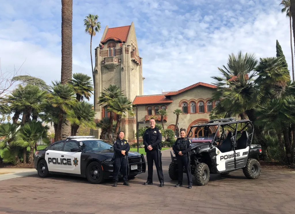 SJSU police officers stand in front of a police car and all-terrain vehicle on campus.
