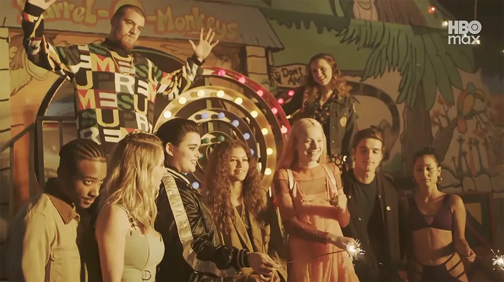 The cast of Euphoria celebrating in front of a carnival-themed backdrop, holding sparklers.