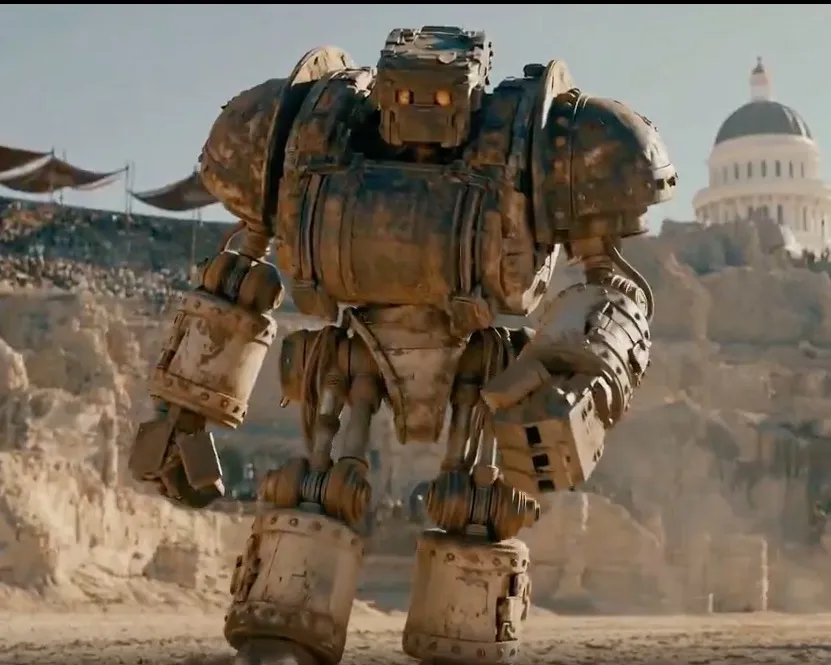 A large, rusty robot stands in a desert landscape with a domed building in the background.