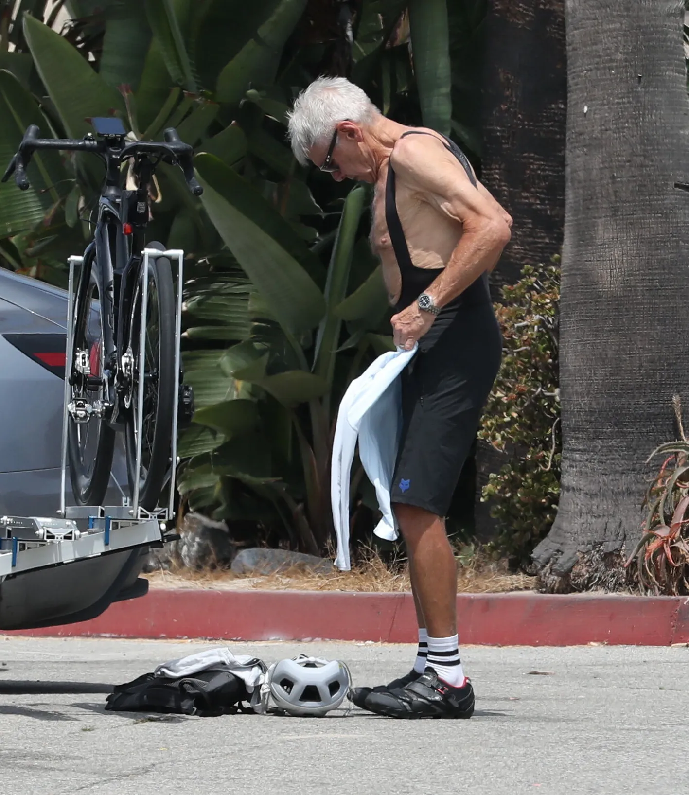 Harrison Ford, in cycling gear, stands by his bike, holding a light blue shirt.