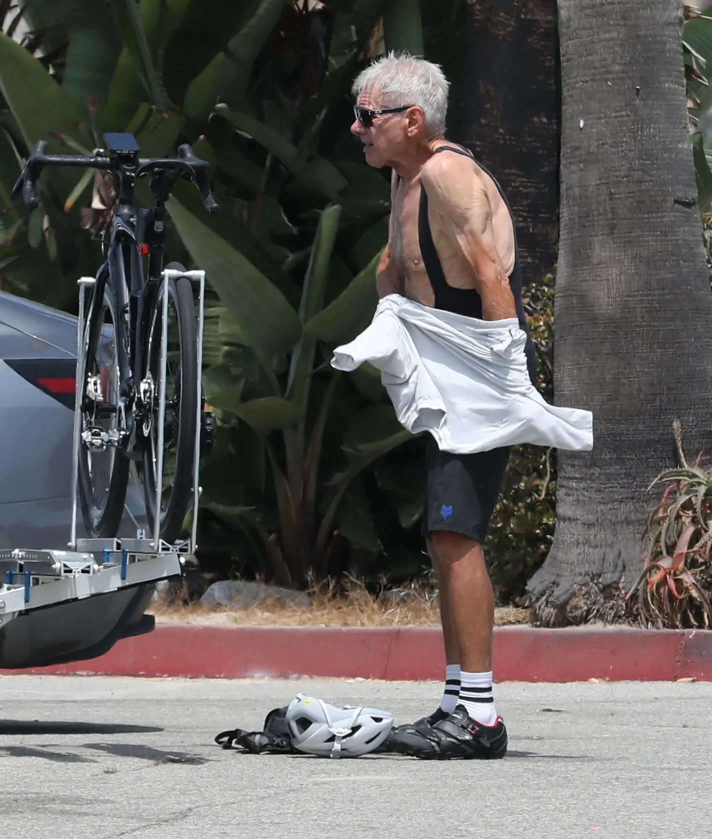 Harrison Ford in cycling gear next to a bike on a rack.