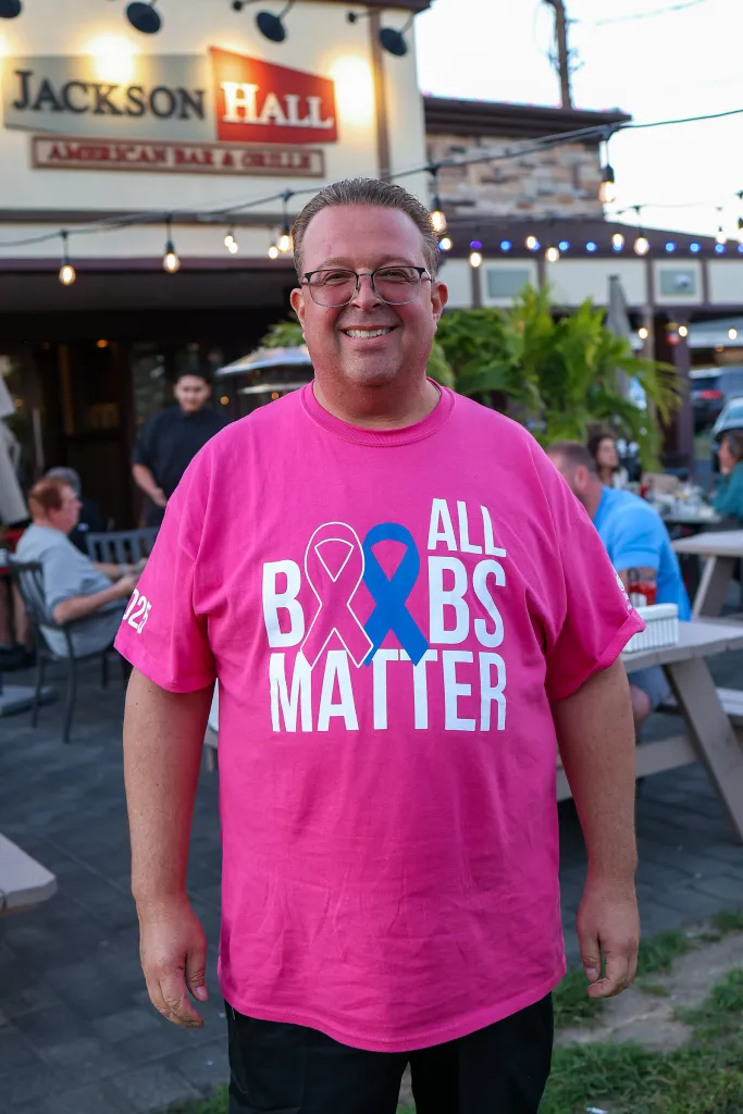 Michael Landesberg, a breast cancer survivor, smiles in front of his restaurant while wearing a pink 