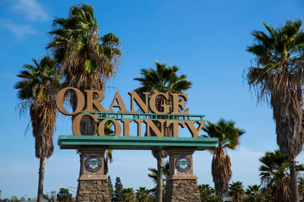 Welcome sign for Orange County, California, with palm trees against a blue sky.