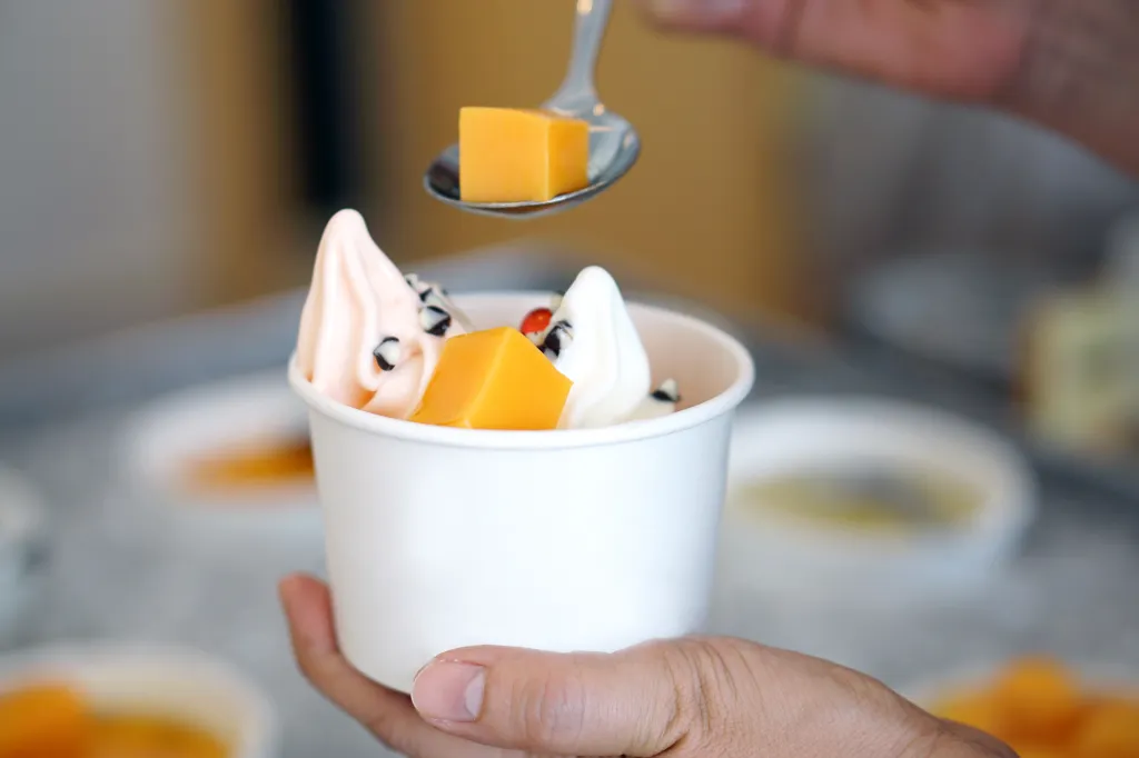 Hand holding a cup of organic frozen yogurt topped with jelly, with a spoon adding another piece of jelly.