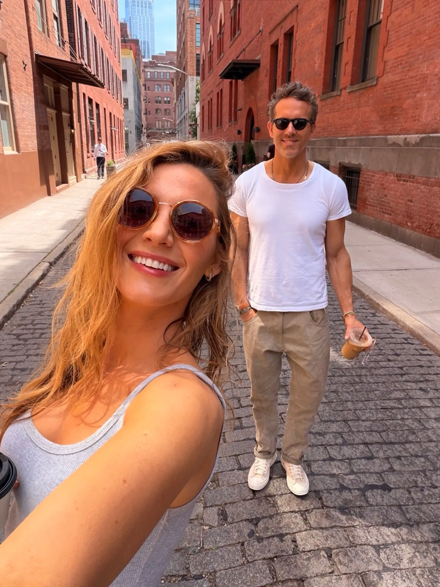 Woman taking a selfie with a man in sunglasses on a cobbled street.