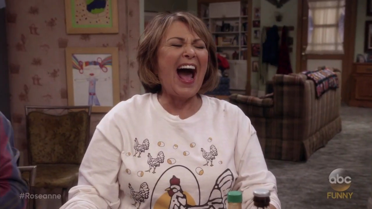 Roseanne Barr, dressed in a chicken-themed shirt, laughs with her mouth wide open.