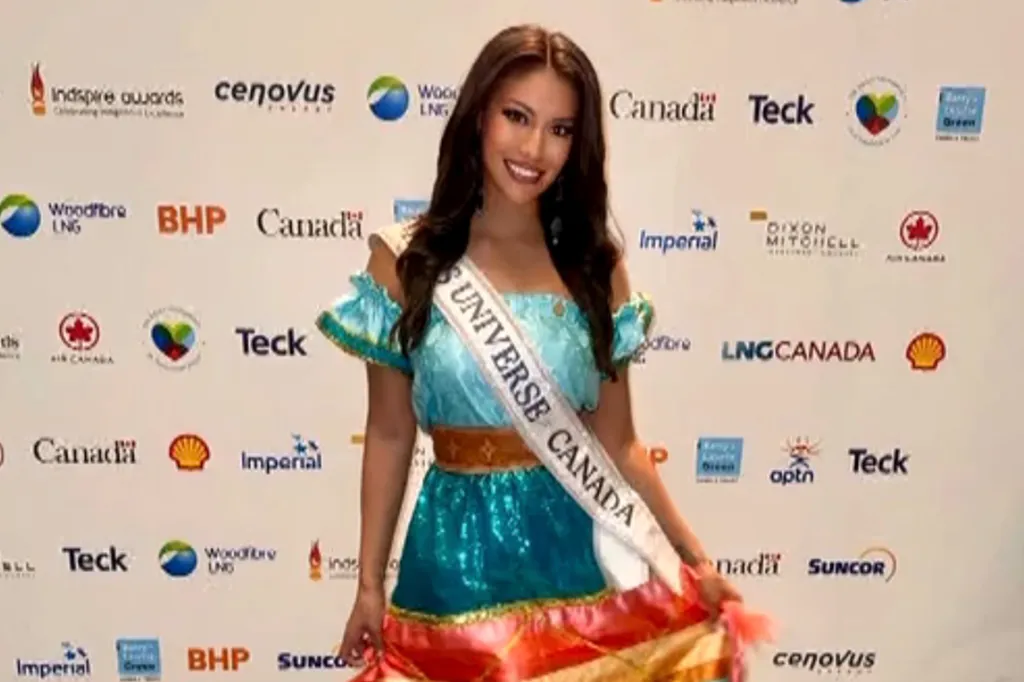 Miss Universe Canada wearing a blue and red dress with a sash, standing against a backdrop of corporate logos.