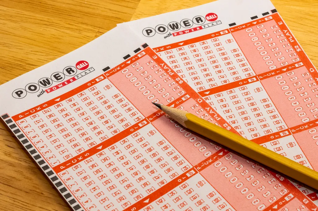 Two blank Powerball lottery play slips with a pencil on a wooden surface.