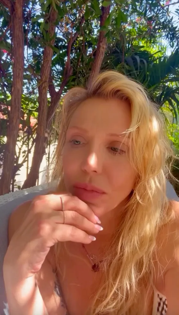 Courtney Love outdoors with her hand under her chin, looking away from the camera.