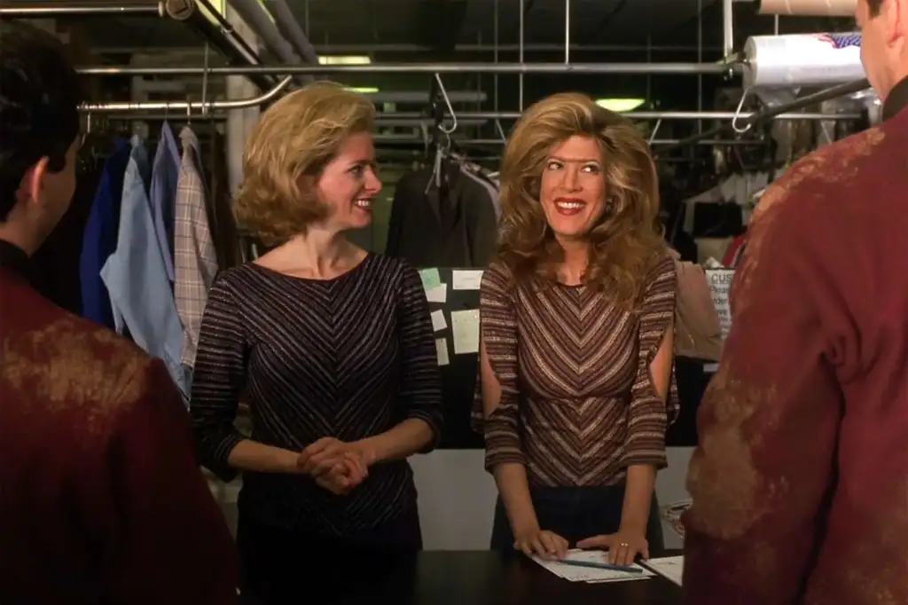 Two women with big hair smiling behind a counter.