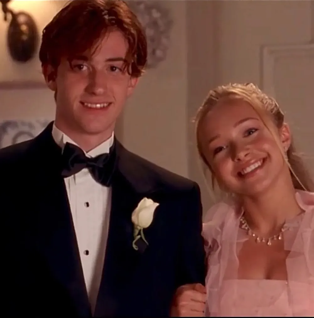 A young man in a black tuxedo and a young woman in a pink dress standing together and smiling.