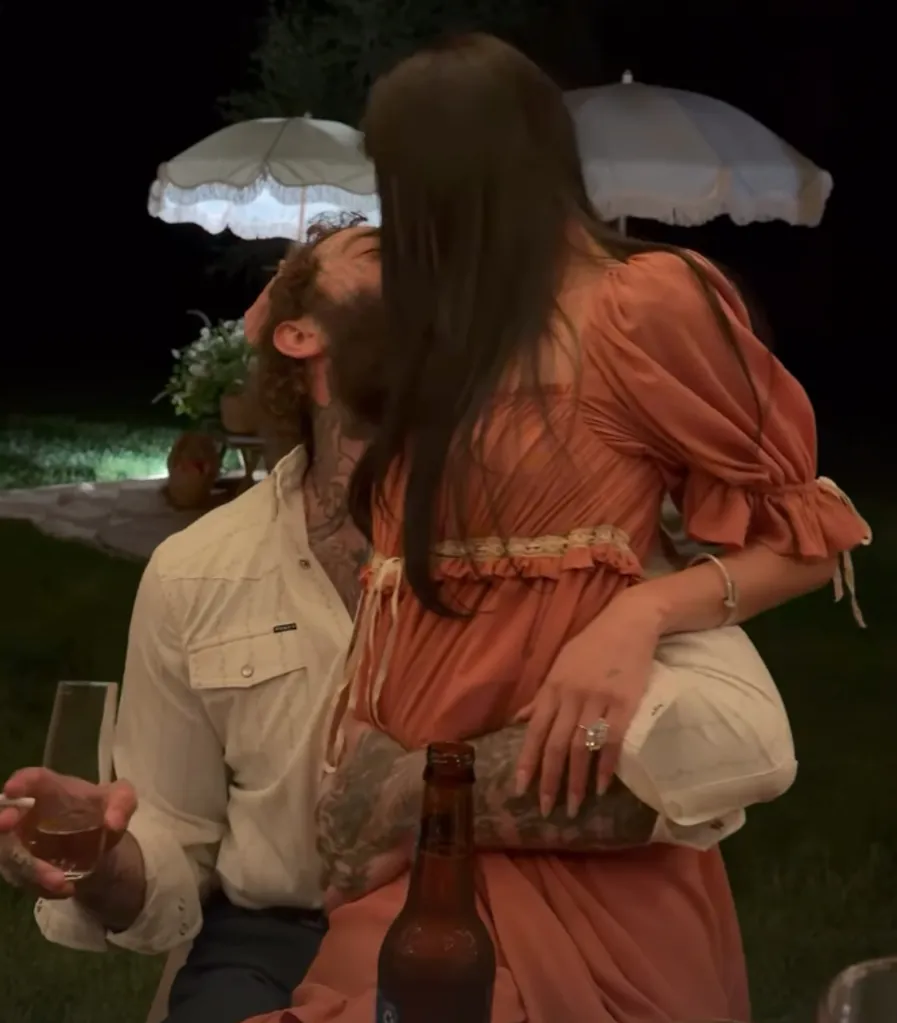 A woman in a long orange dress sitting on a man's lap and kissing him.